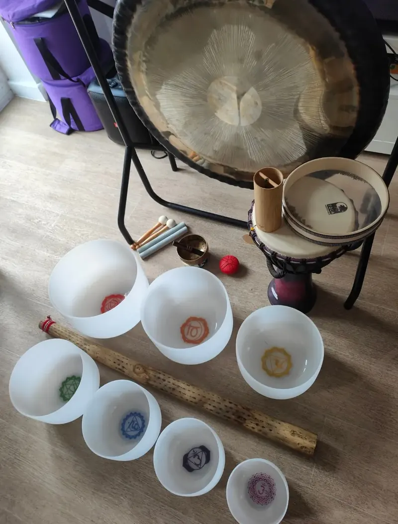 Crystal singing bowls with chakra symbols in front of a planetary gong, with a rainstick, ocean drum, koshi chime and mallets