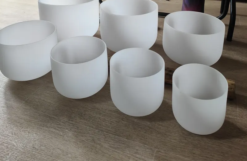Seven frosted quartz crystal singing bowls of different sizes on a wooden floor