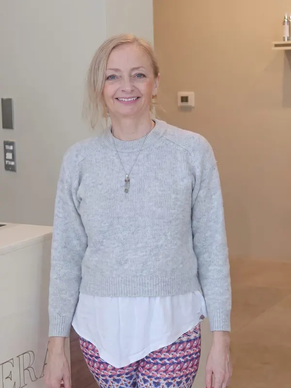 Patsy, smiling, in a grey jumper and patterned leggings at the clinic